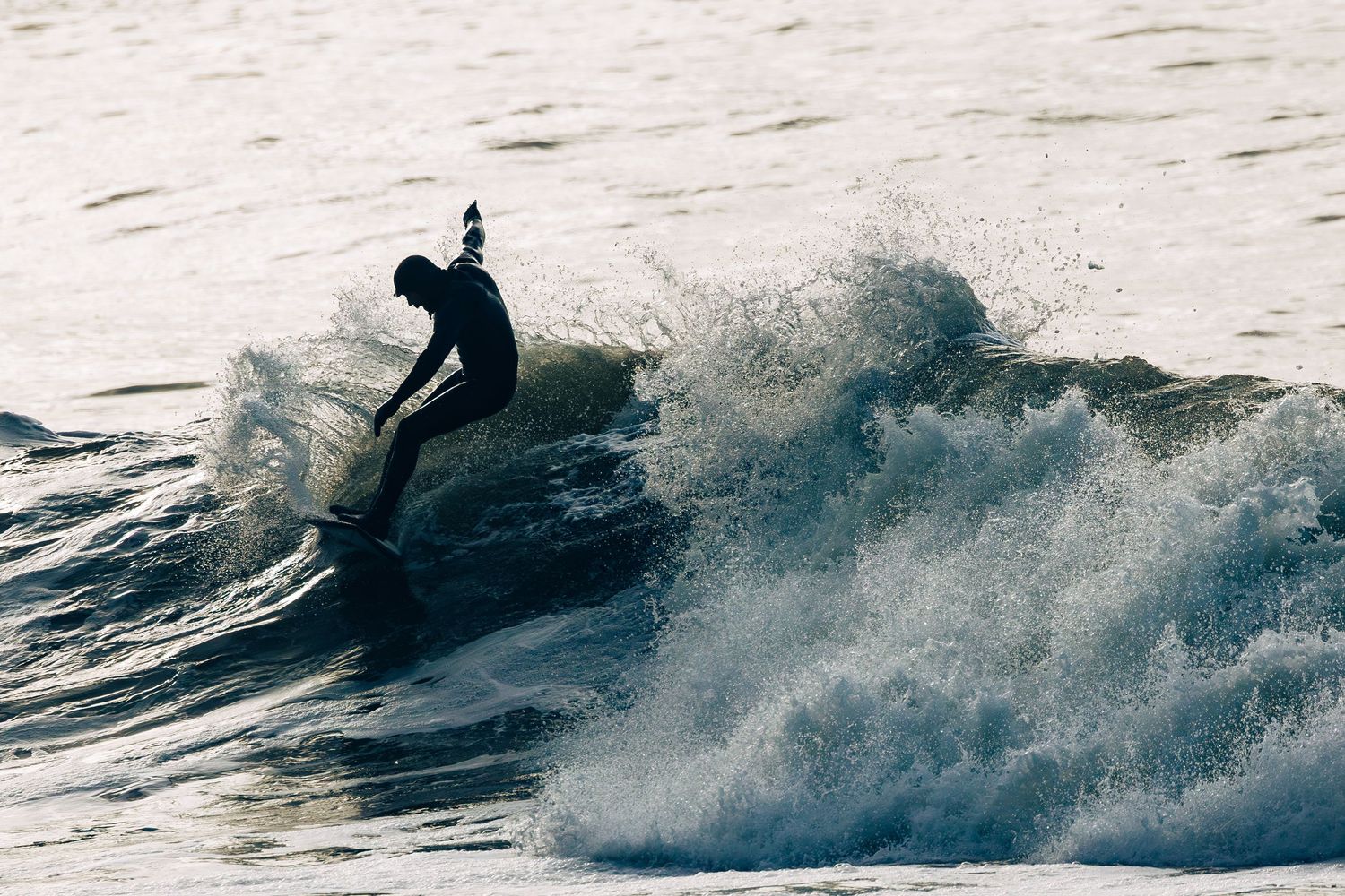 A surfer rides a powerful ocean wave while kicking up spray during sunset on Vancouver Island.