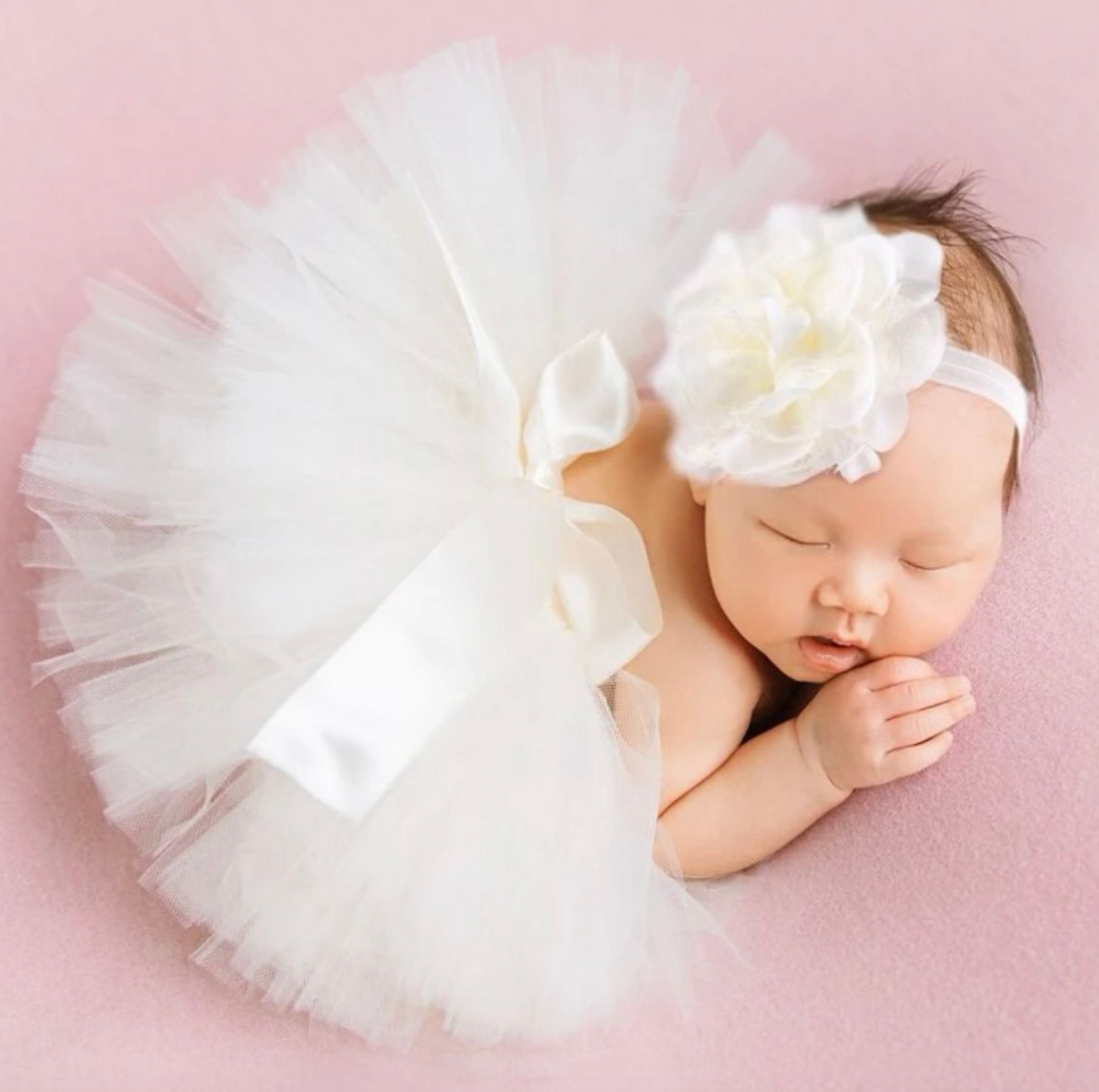 Sweet newborn photography setup with white tulle tutu and bow on soft pink background.