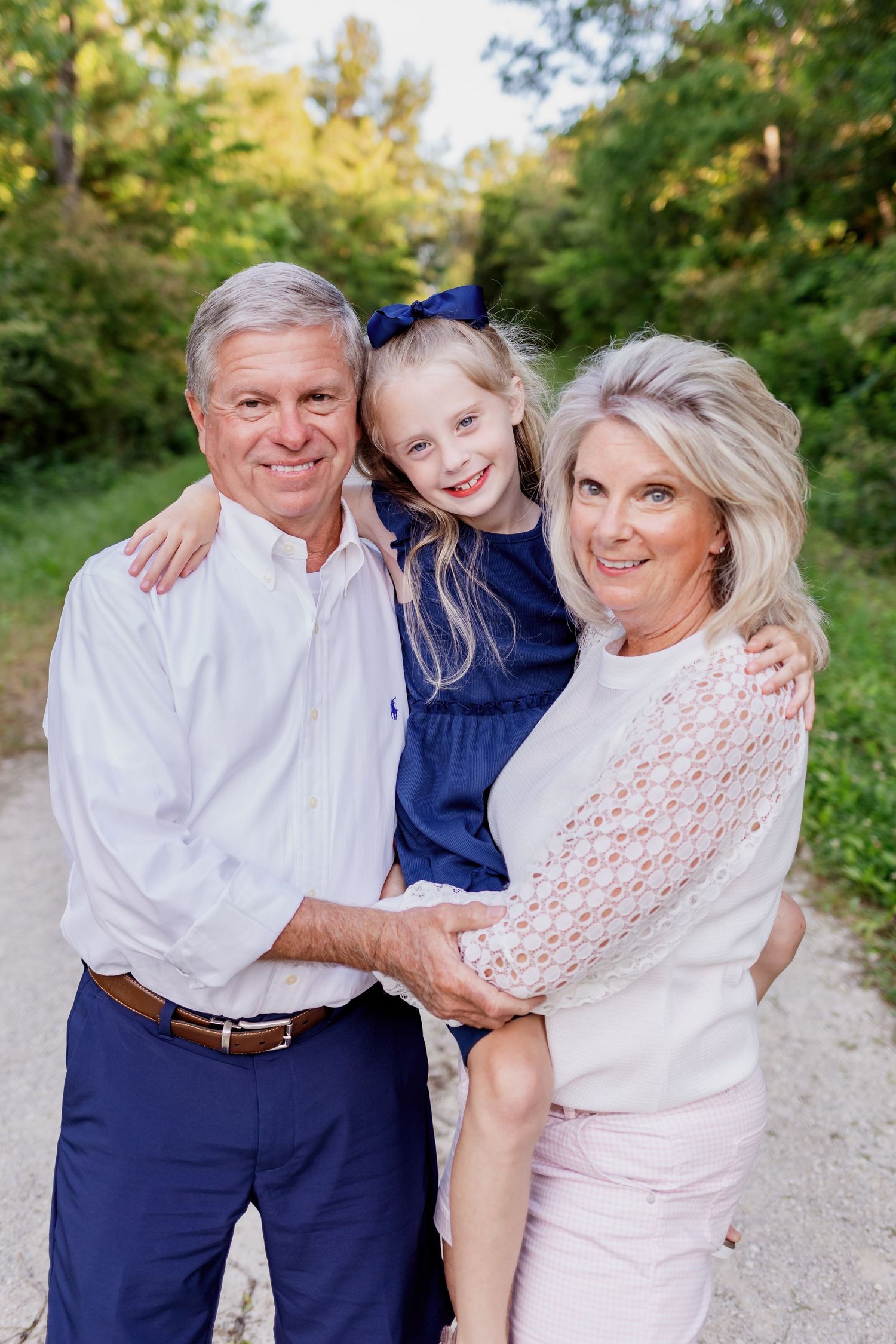 Family portrait of three people in coordinated blue and white outfits on outdoor path.