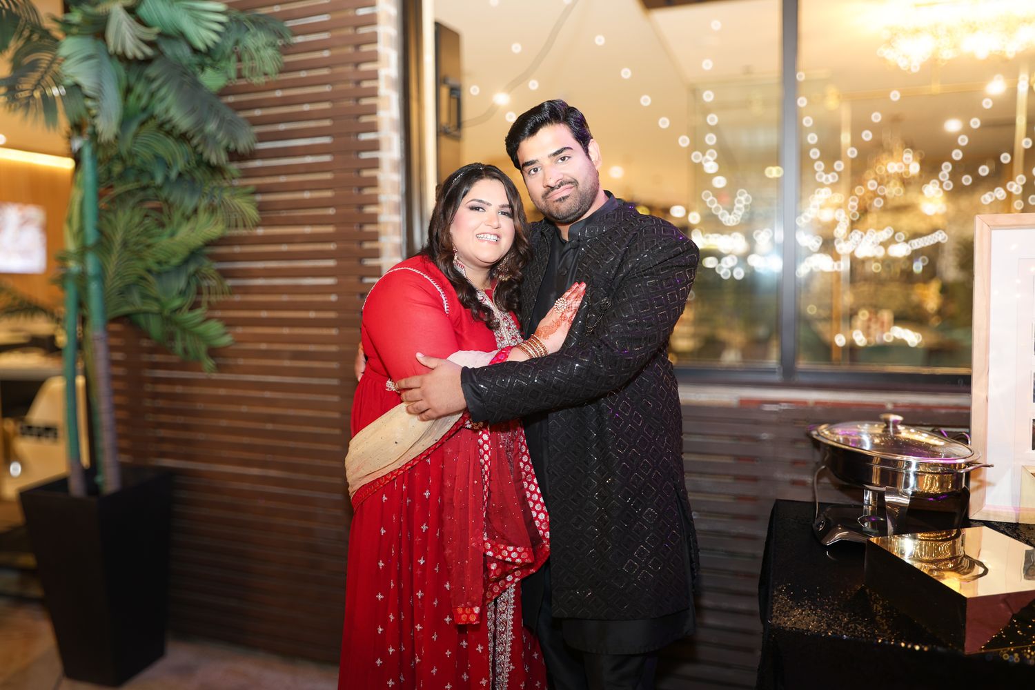 Couple dancing together at an evening celebration with decorative lighting in background.