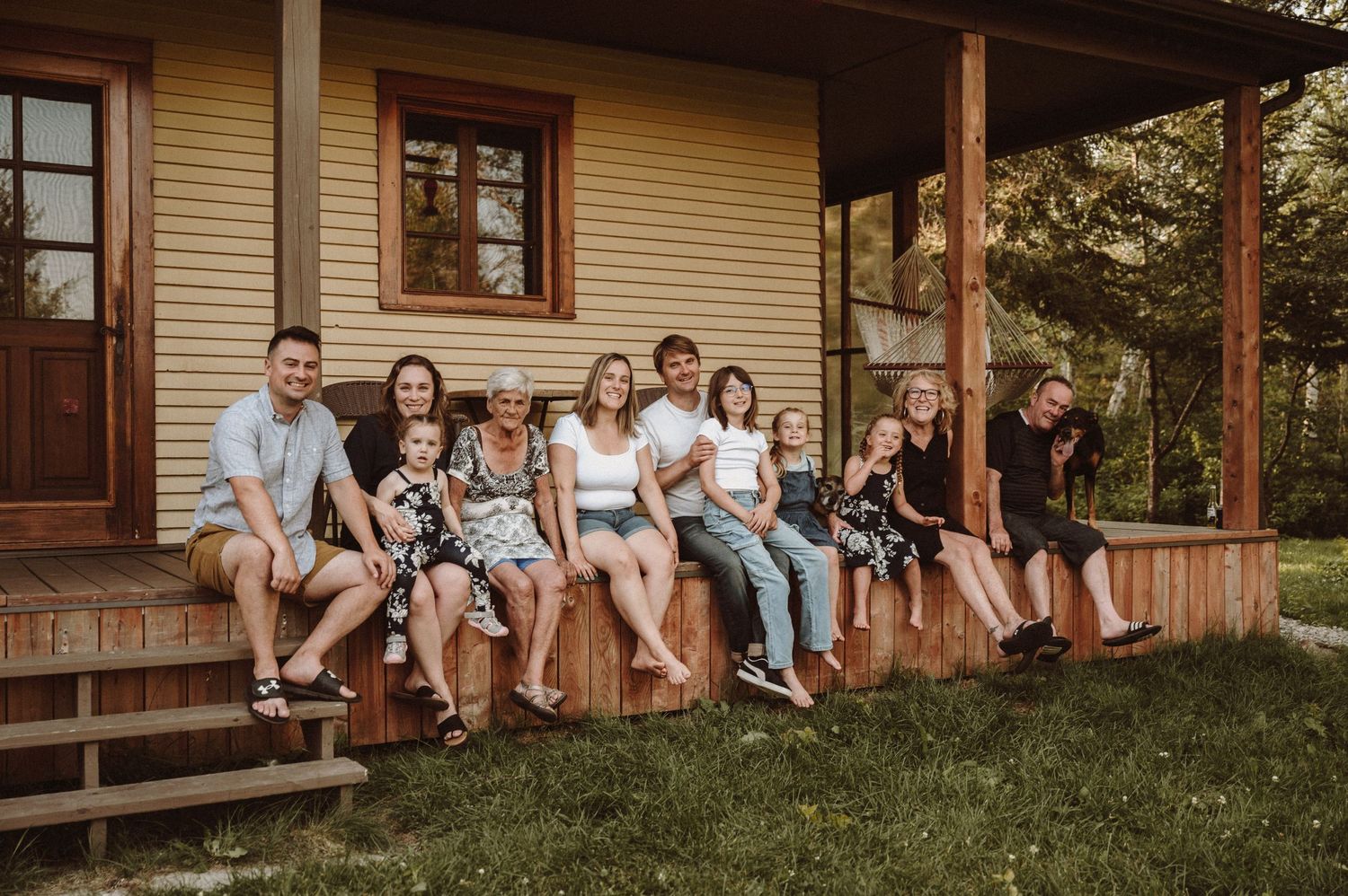 Extended family sitting together on wooden porch steps of country house.