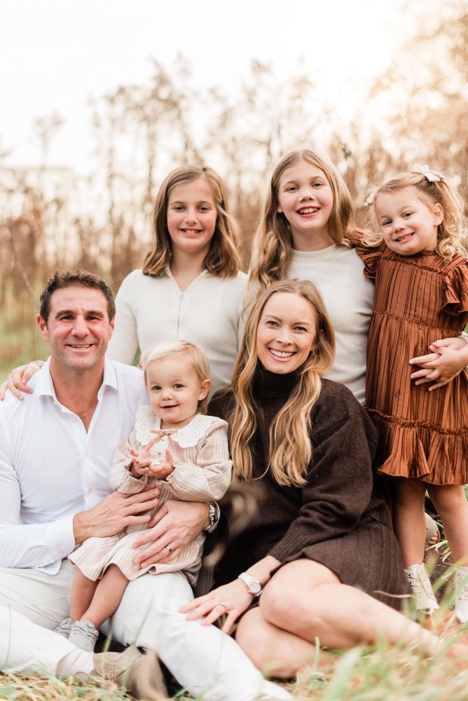 Family portrait outdoors with parents and children sitting together in warm autumn light.