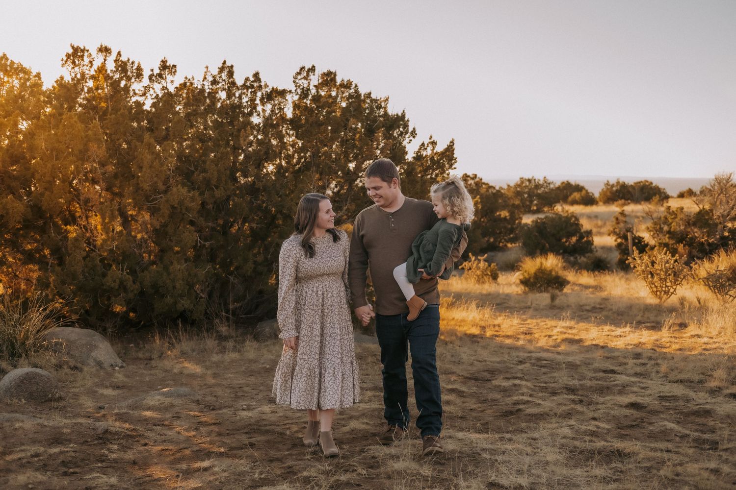 A family stands together during golden hour in the sandia foothills with sunlit brush behind them. Family photo session outfit inspiration.