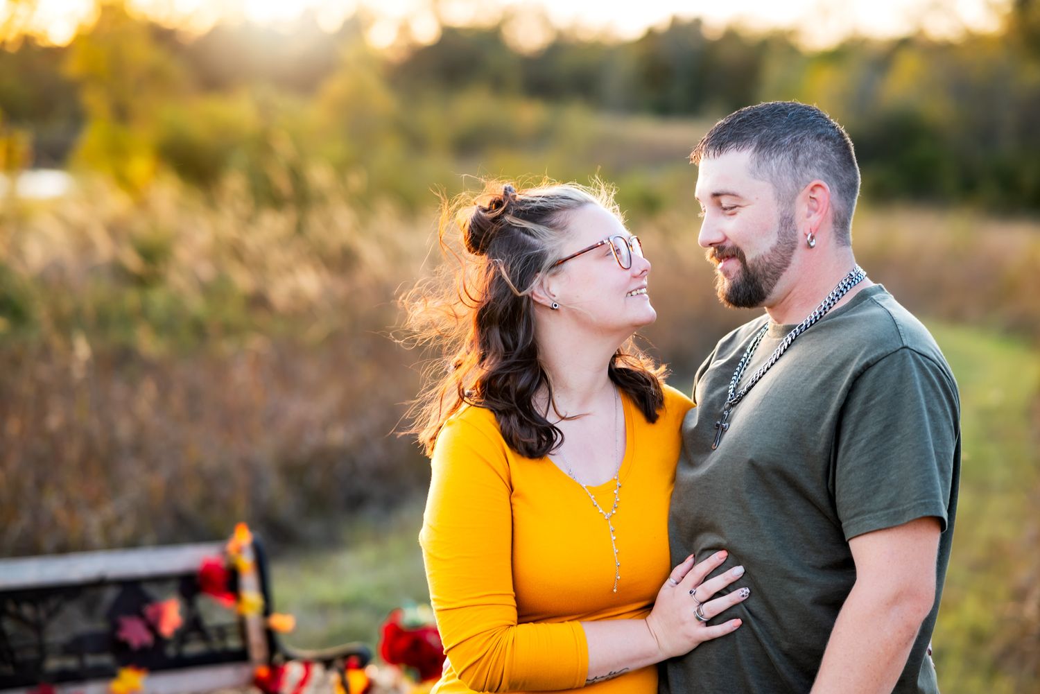 Couple laughing together outdoors at sunset with autumn pumpkins visible in background.