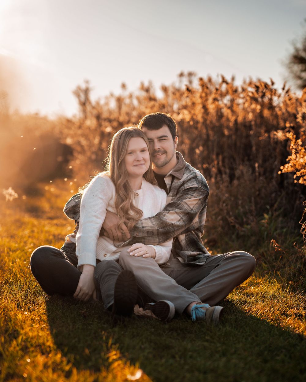 Couple sitting together on grass at sunset surrounded by golden autumn foliage.