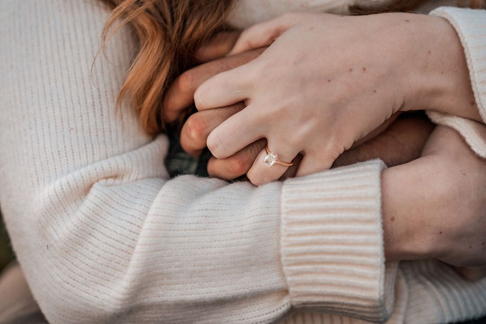 Close-up shot of hands wearing a white knit sweater with engagement ring detail.