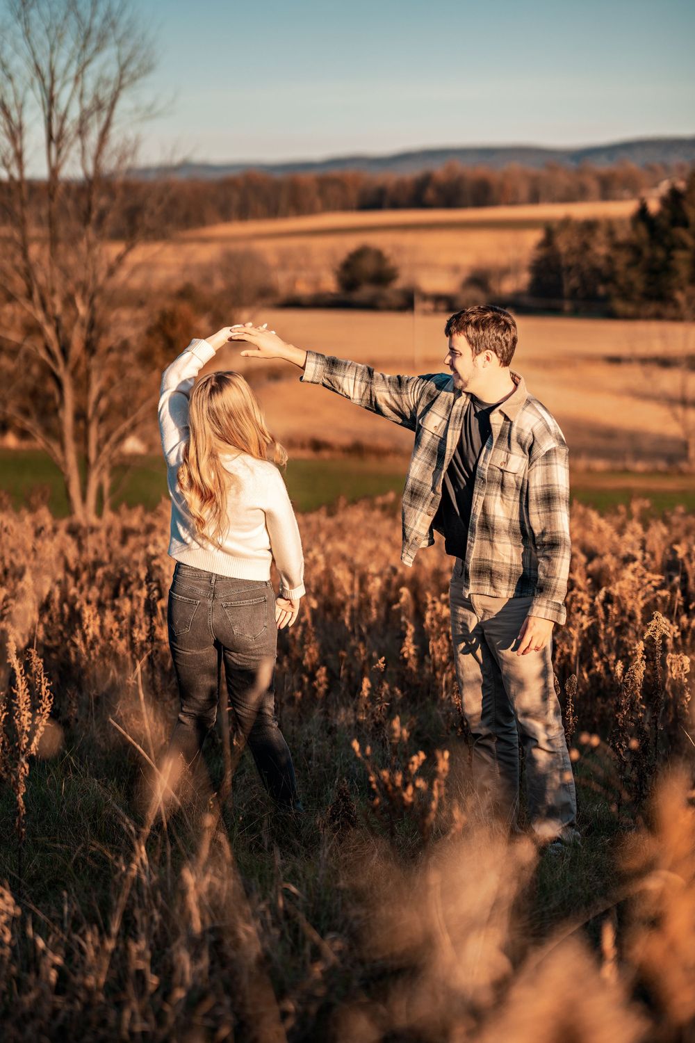 A couple dancing in a golden field during sunset with rolling hills in the background.