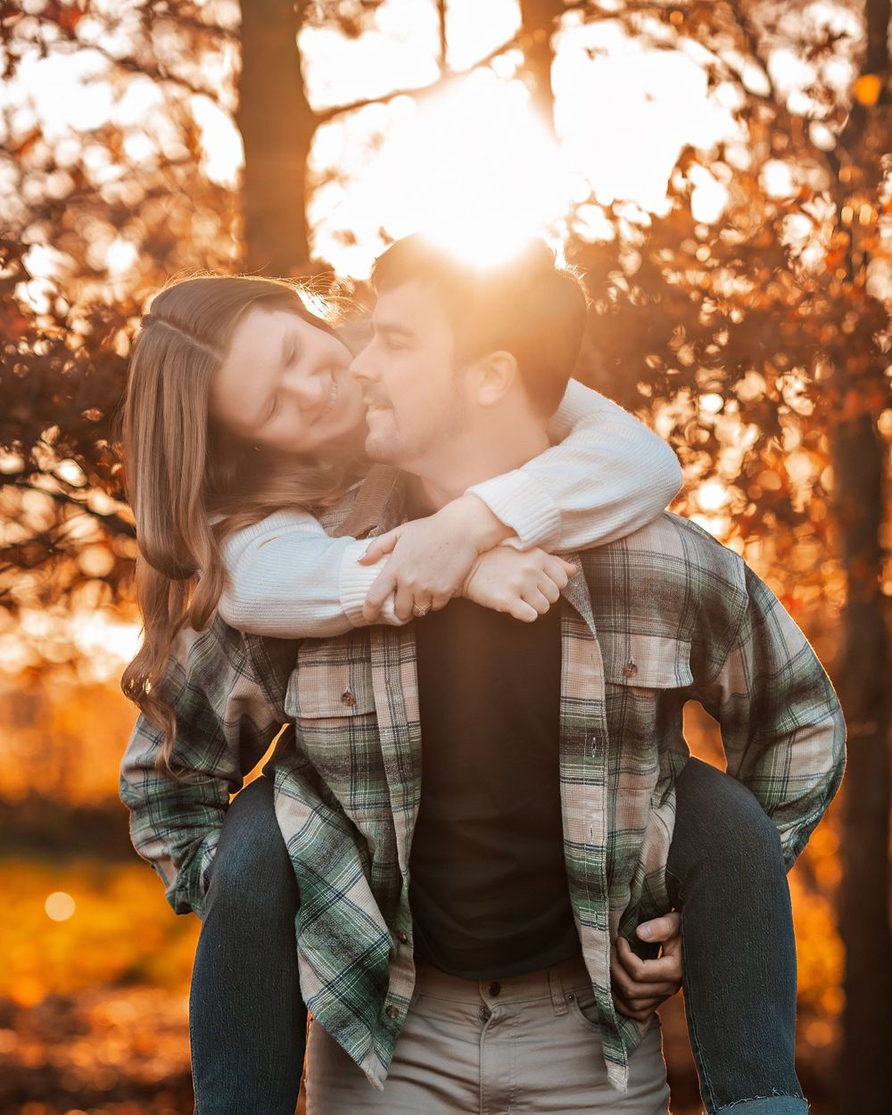 Romantic couple sharing playful piggyback moment in golden sunset light through autumn trees.