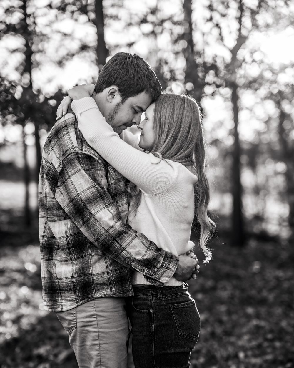A romantic embrace between a couple in a forest wearing casual fall attire.
