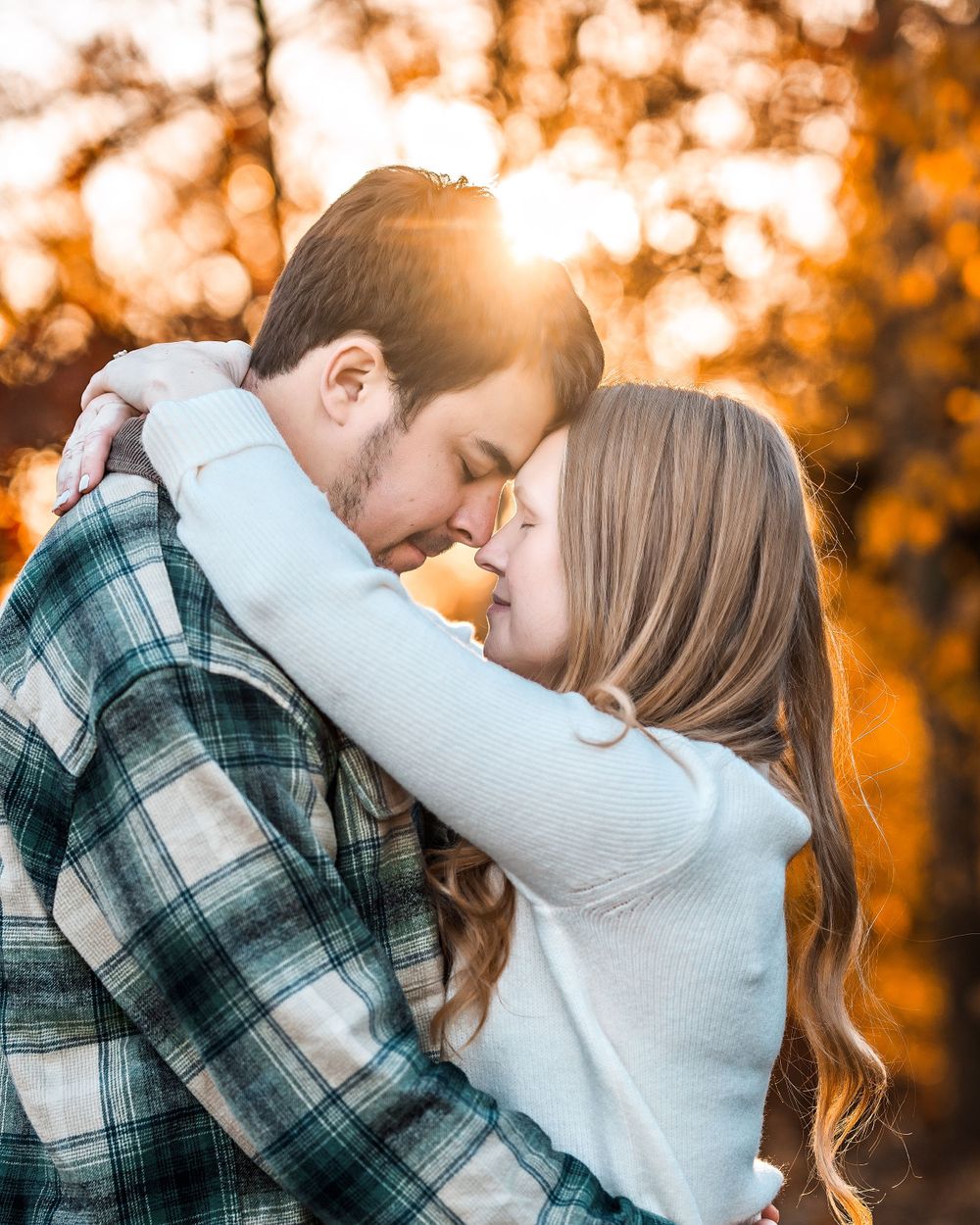 Romantic couple embraces in warm autumn sunset light with golden bokeh through trees in background.