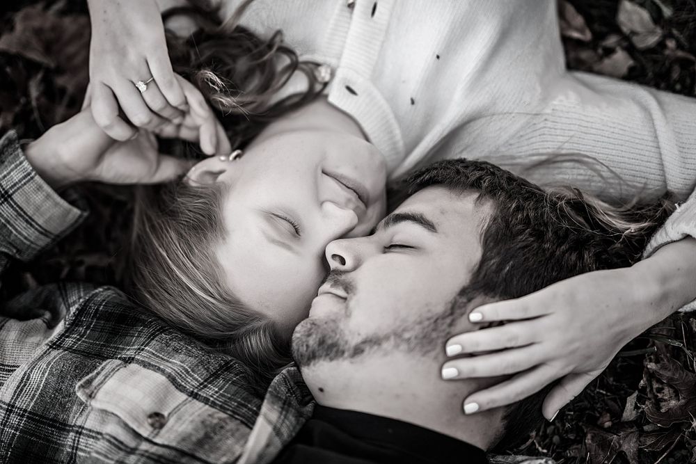 Couple lying together on autumn leaves in black and white photograph.