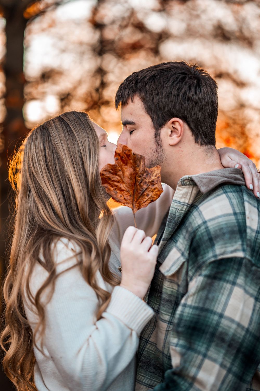 A couple shares an intimate autumn moment with a maple leaf between them.