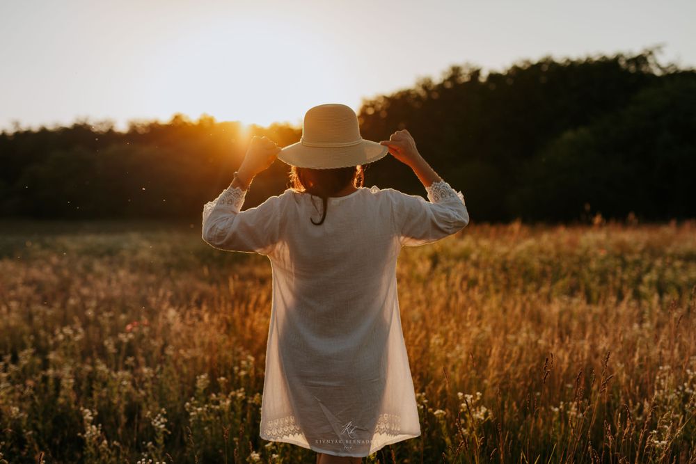 Silhouette of someone wearing a hat and white shirt against a golden sunset in a field.