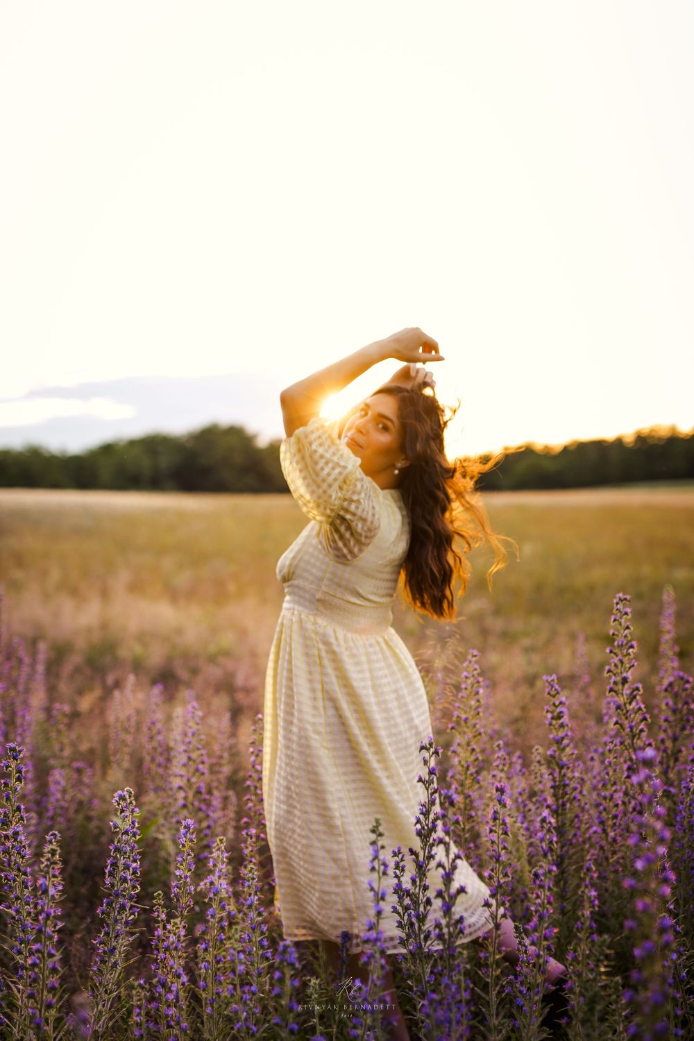 Woman in white dress twirling in a field of purple wildflowers at sunset.