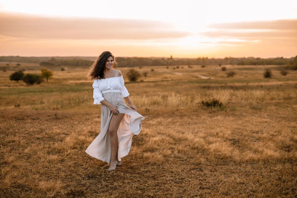Ethereal figure in white dress twirls in golden field during sunset.