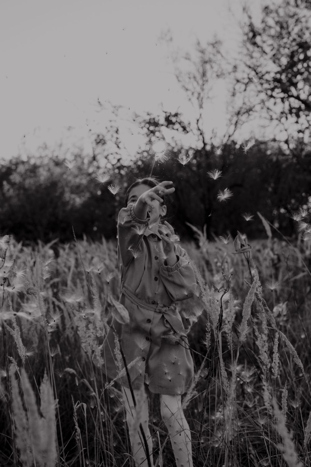 Black and white image of figure standing in tall grass with trees in background.