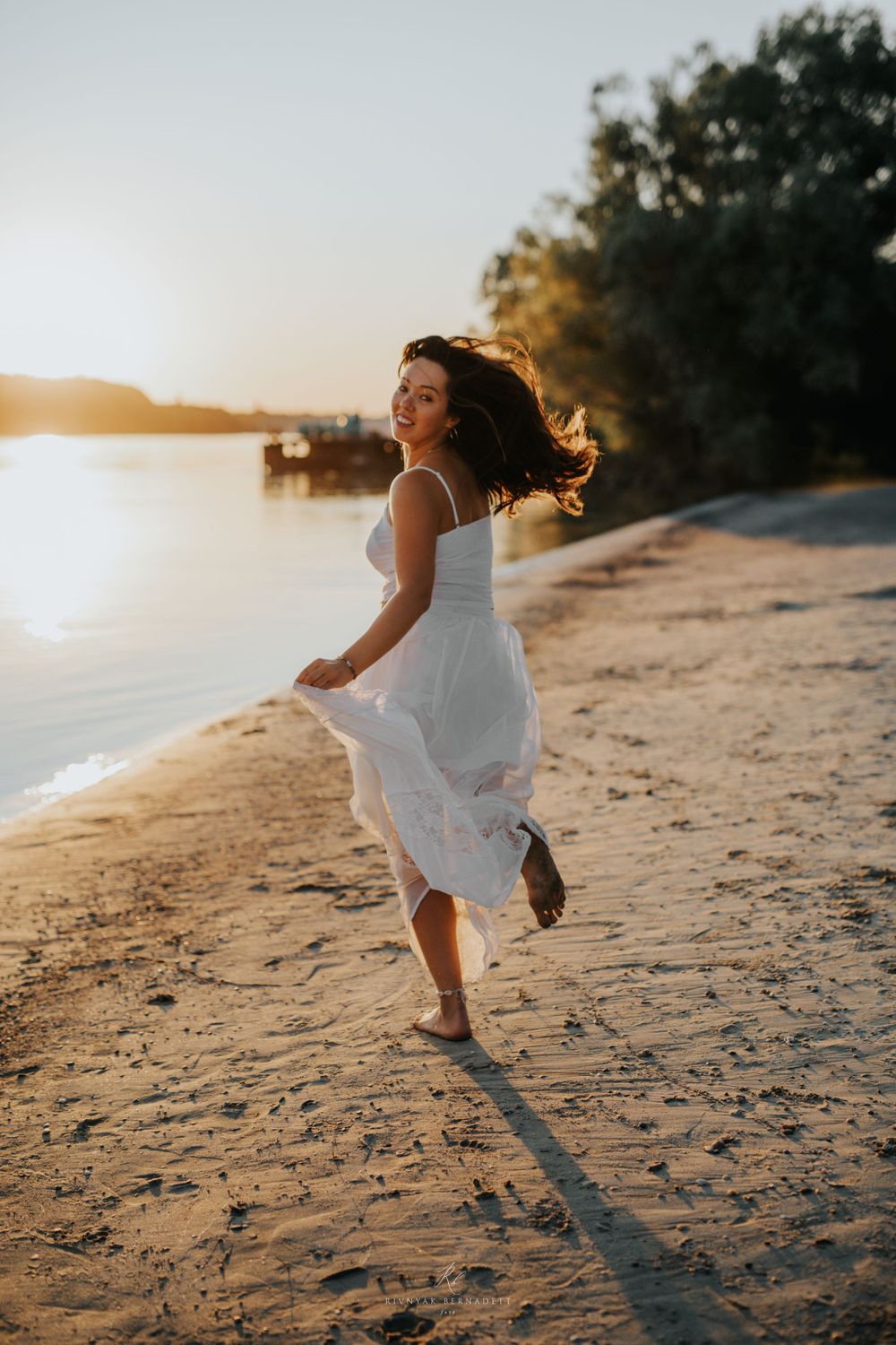 Woman in white dress twirling on beach at sunset with flowing fabric and hair.