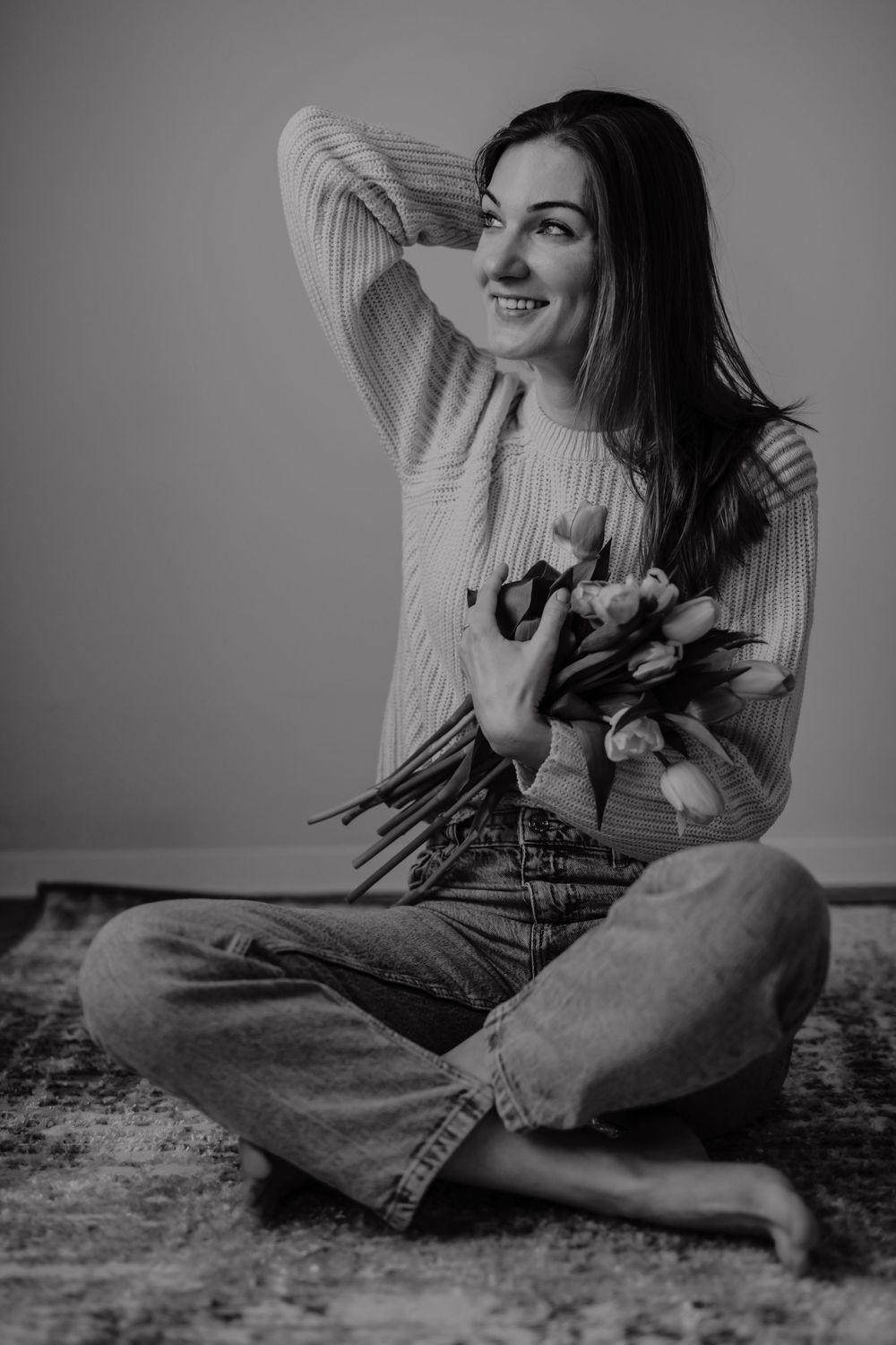 Person in knit sweater holding flowers while sitting cross-legged.