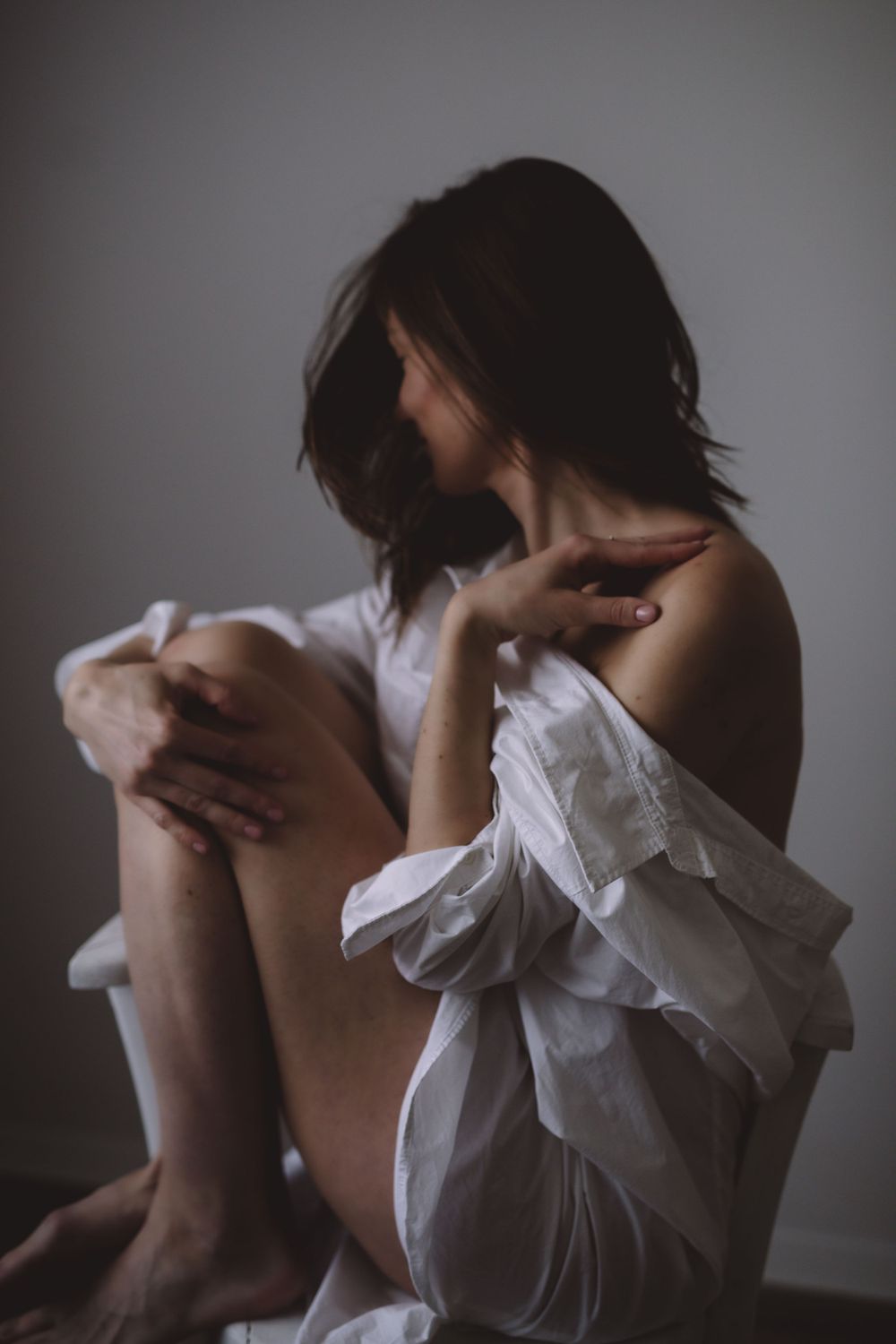 Artistic portrait of person in white blouse sitting with dramatic lighting.