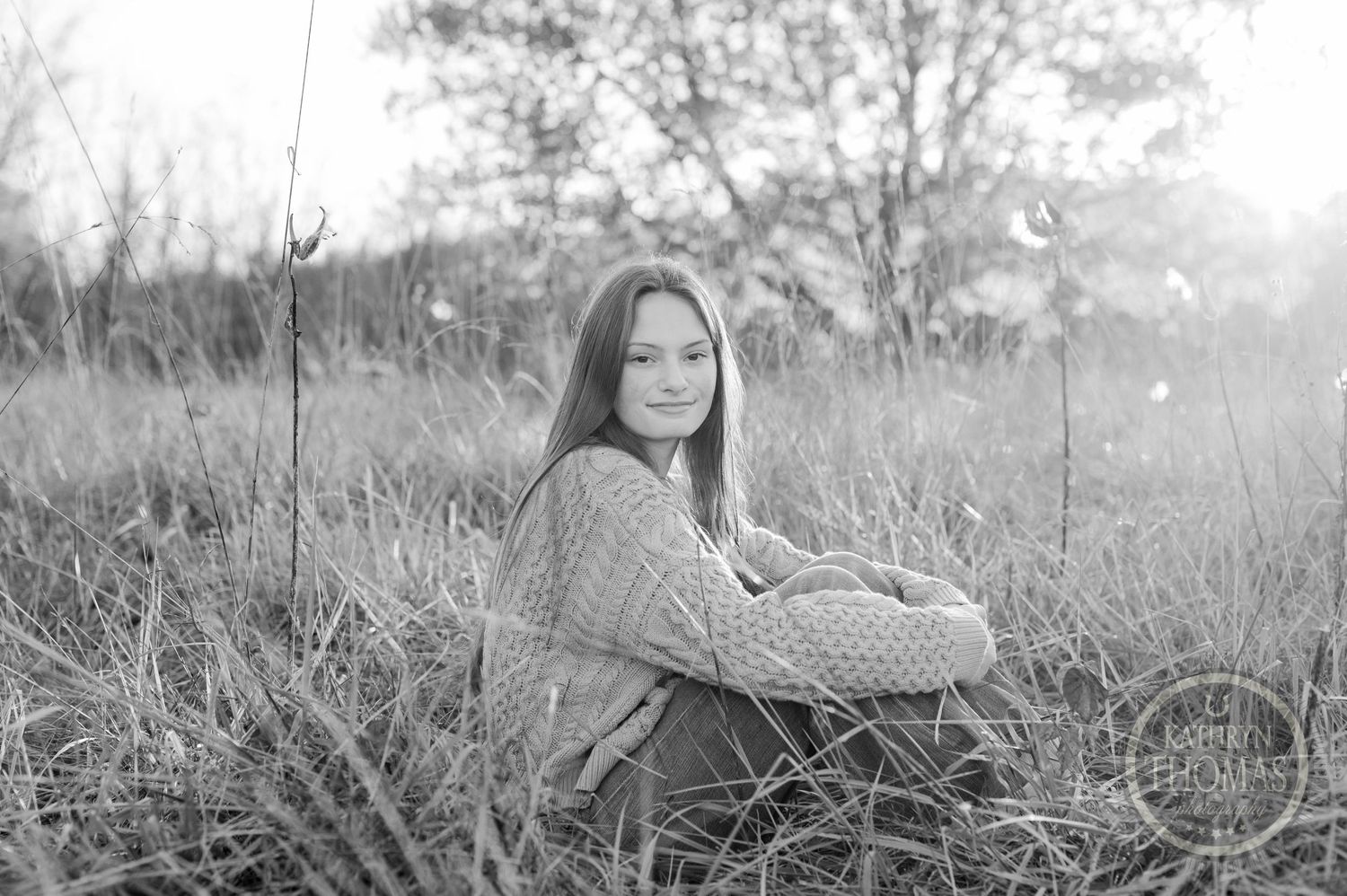 A dreamy black and white portrait of someone sitting in tall grass during golden hour.