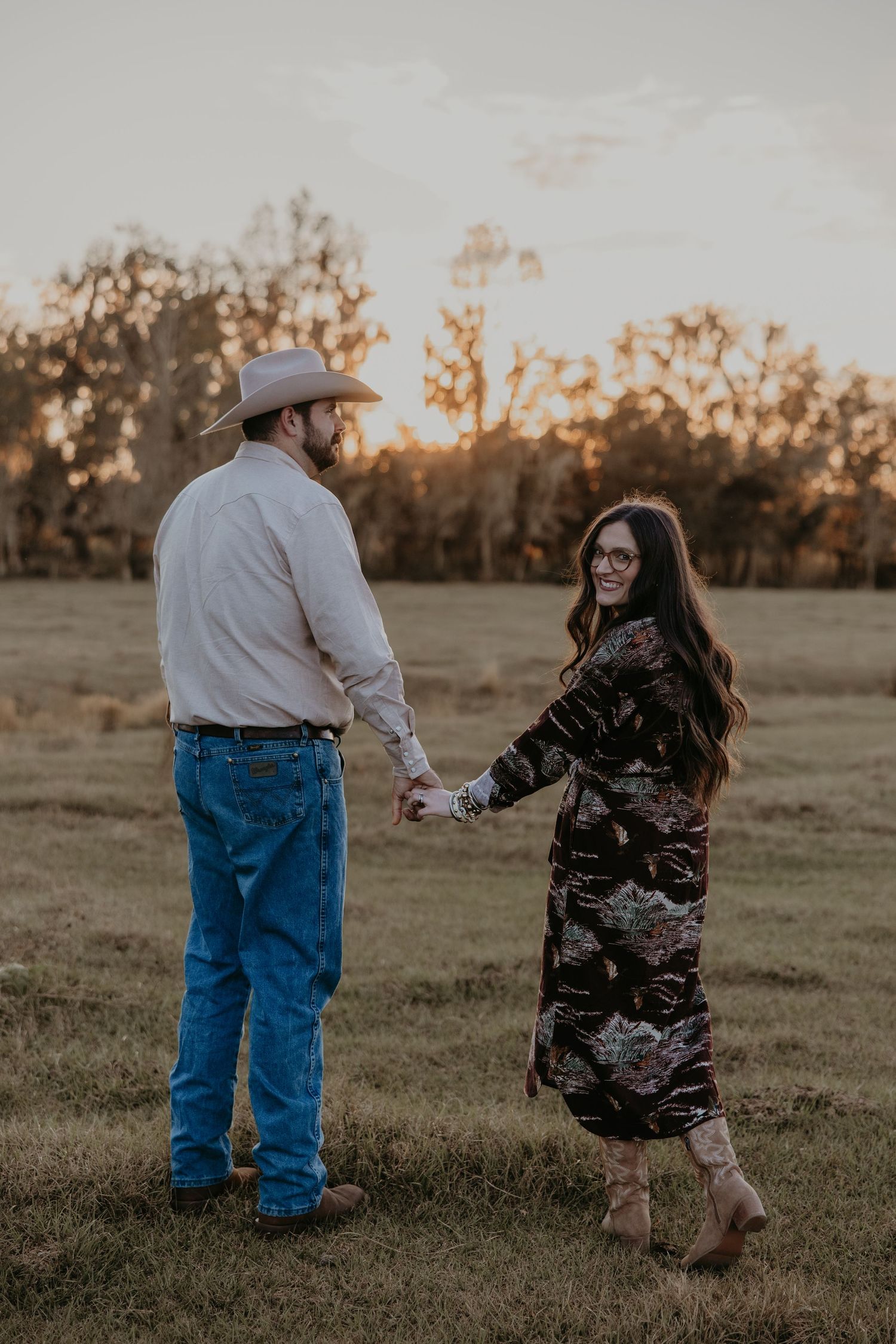 A romantic sunset embrace between newlyweds wearing cowboy hats in a golden field.