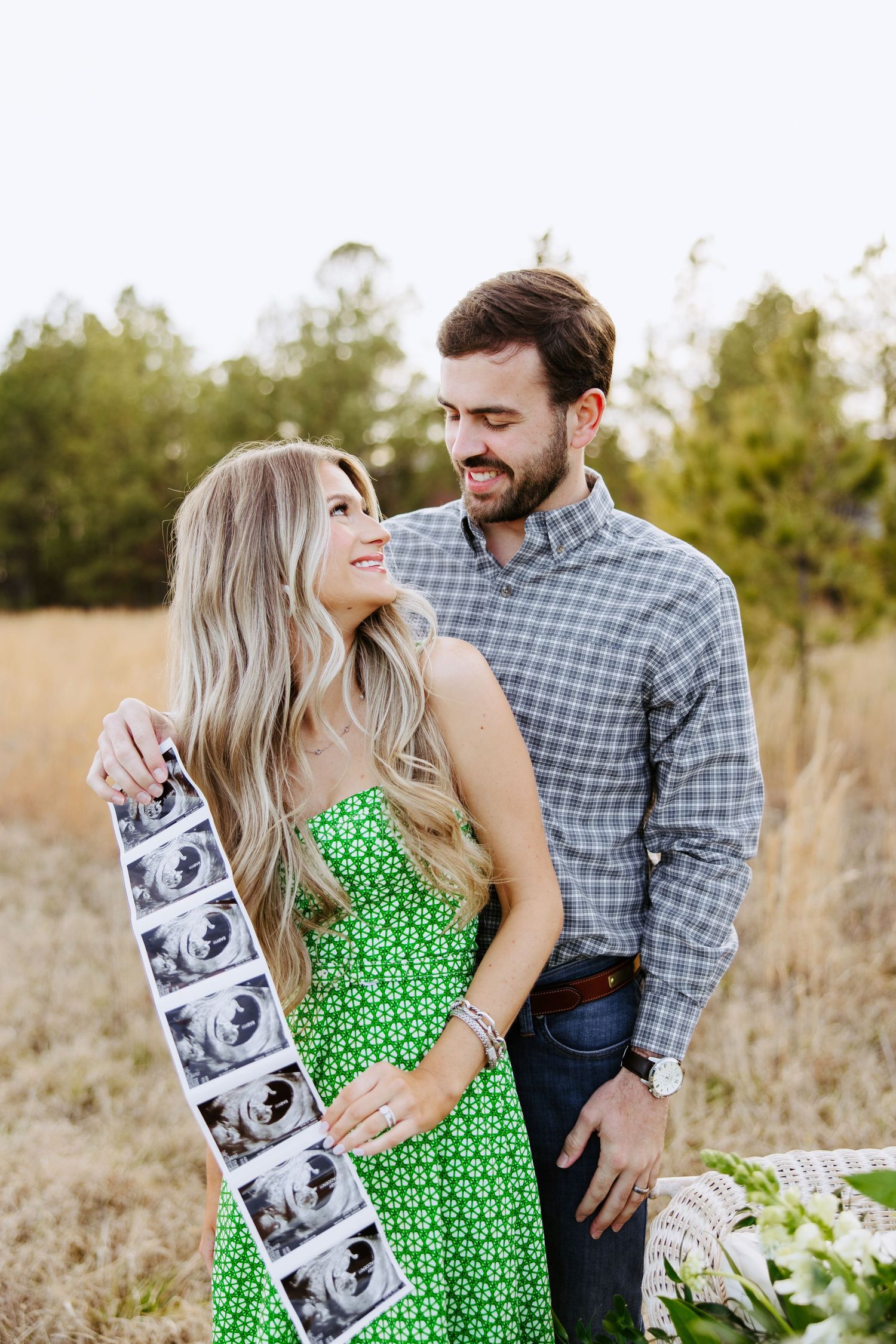 Couple in field sharing ultrasound photos and smiling while celebrating pregnancy announcement outdoors.