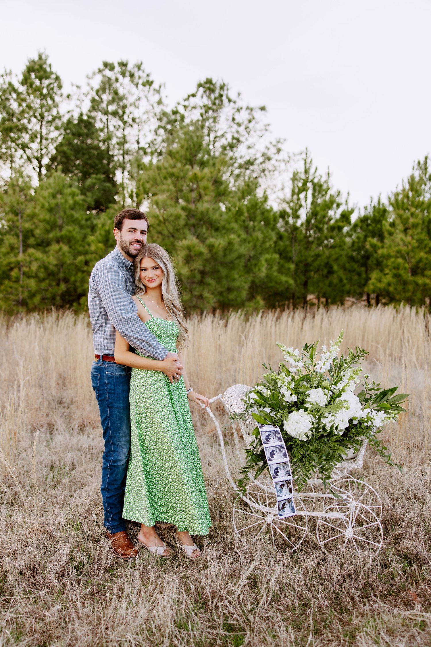 A couple embraces in a field of tall grass next to a vintage bicycle decorated with white floral arrangements.
