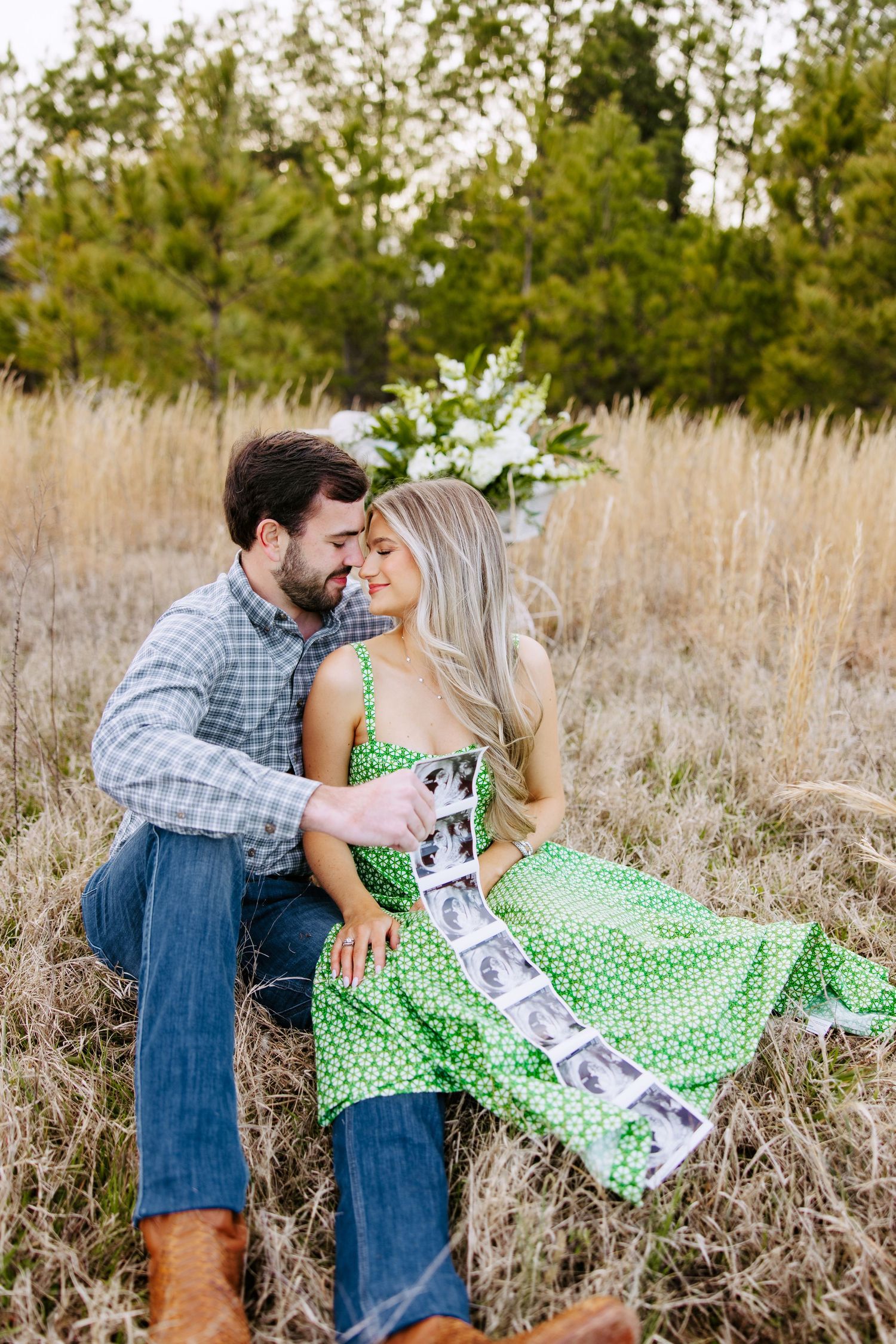 A couple shares a romantic moment in a field of tall grass and wildflowers wearing casual attire on a sunny day.