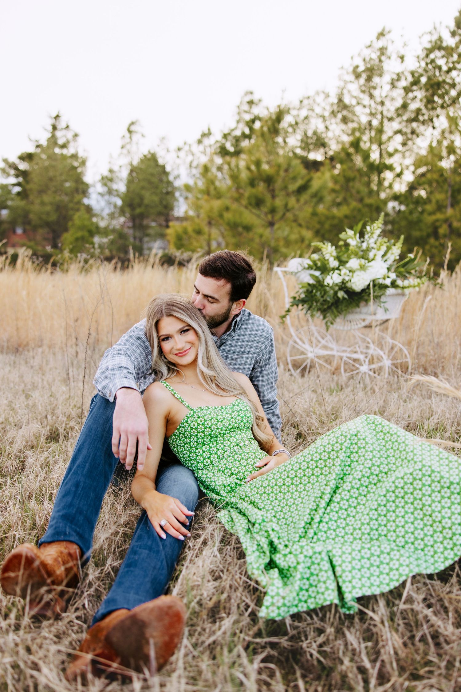 A couple sits together in a field of tall grass, with her wearing a flowing green polka dot dress.