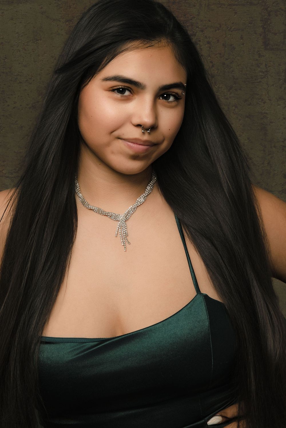 Portrait of someone in a green satin camisole with long dark hair and a delicate silver necklace against a dark background.