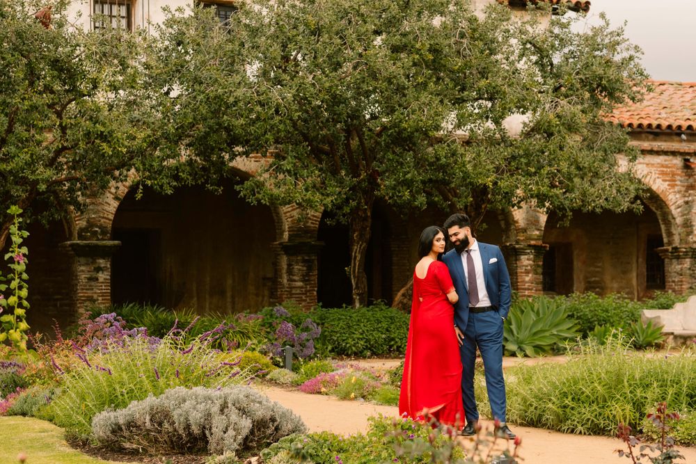A couple stands in a garden courtyard with stone arches and blooming flowers at an elegant Spanish-style venue.