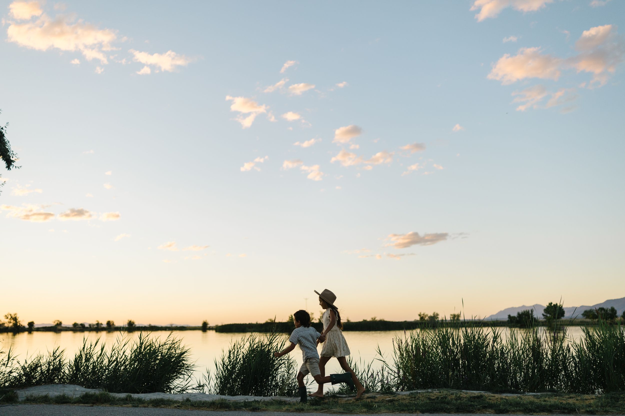 Silhouette figures stand along a tranquil lake shore during a peaceful sunset with wispy clouds above.