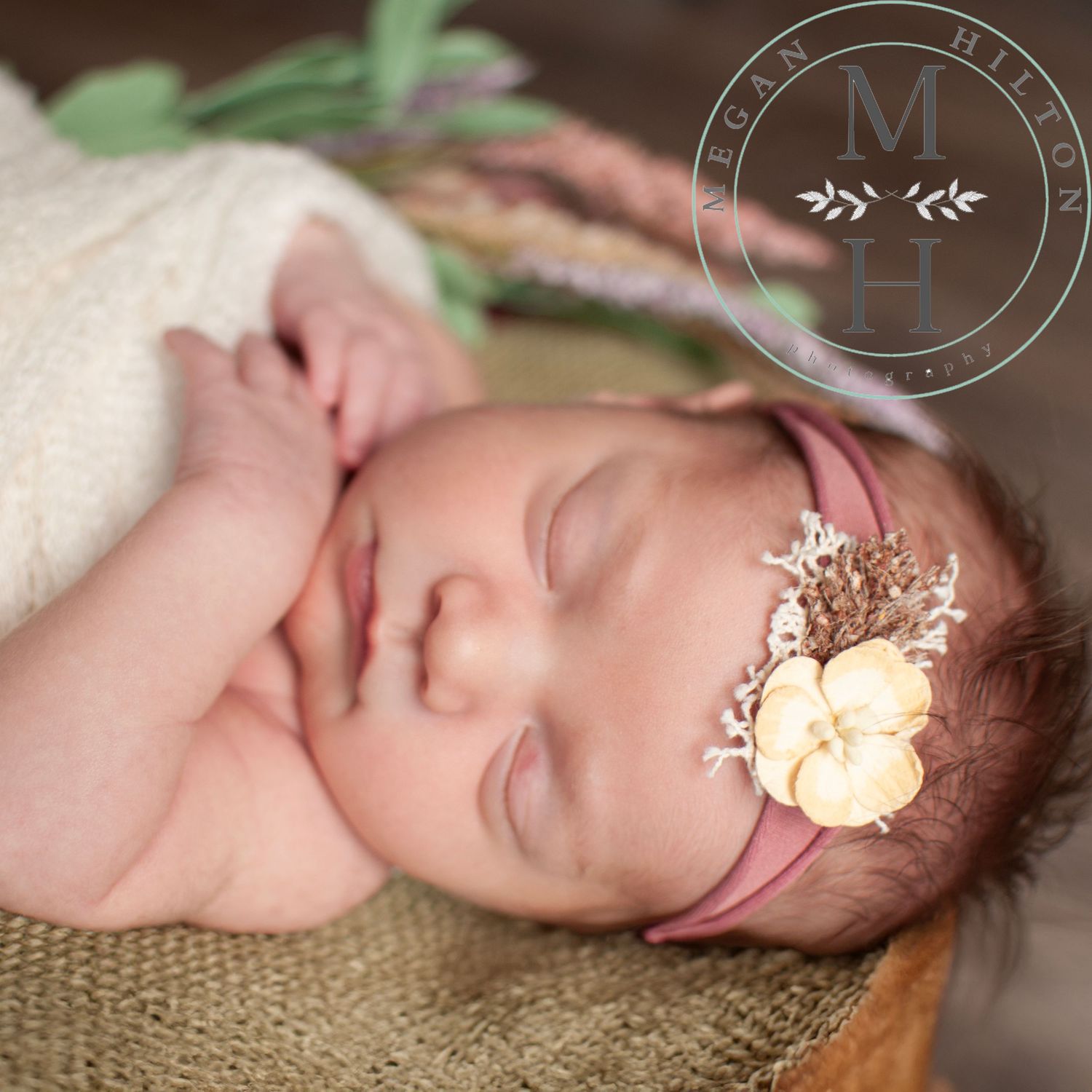 Close up photo of a newborn wearing delicate floral headband and wrapped in soft cream blanket on burlap background.