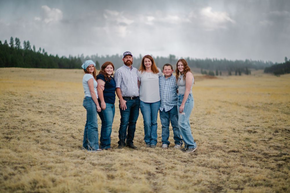 Family group poses together in an open field with mountains in background.