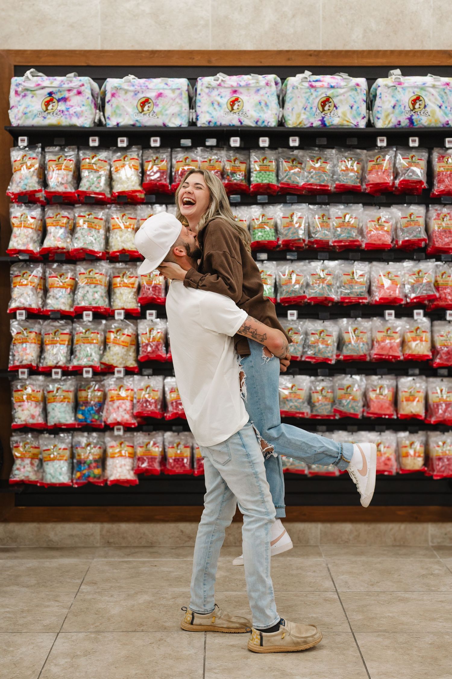 Playful couple embraces in front of colorful pet food display at store.