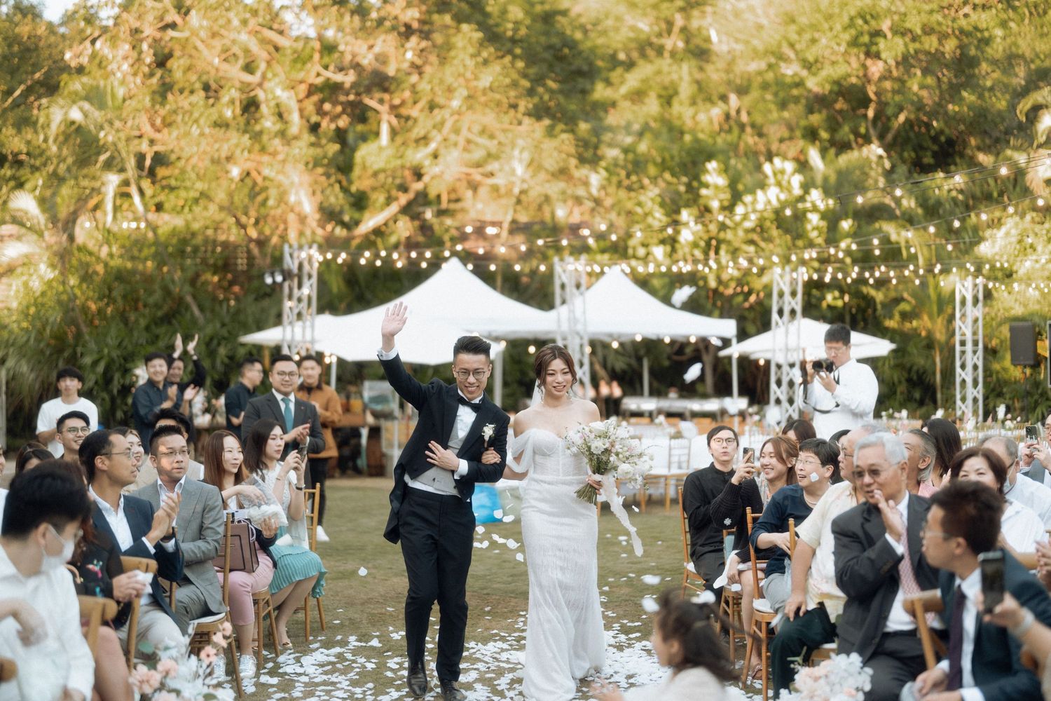 Outdoor wedding celebration with confetti under white tent and trees.