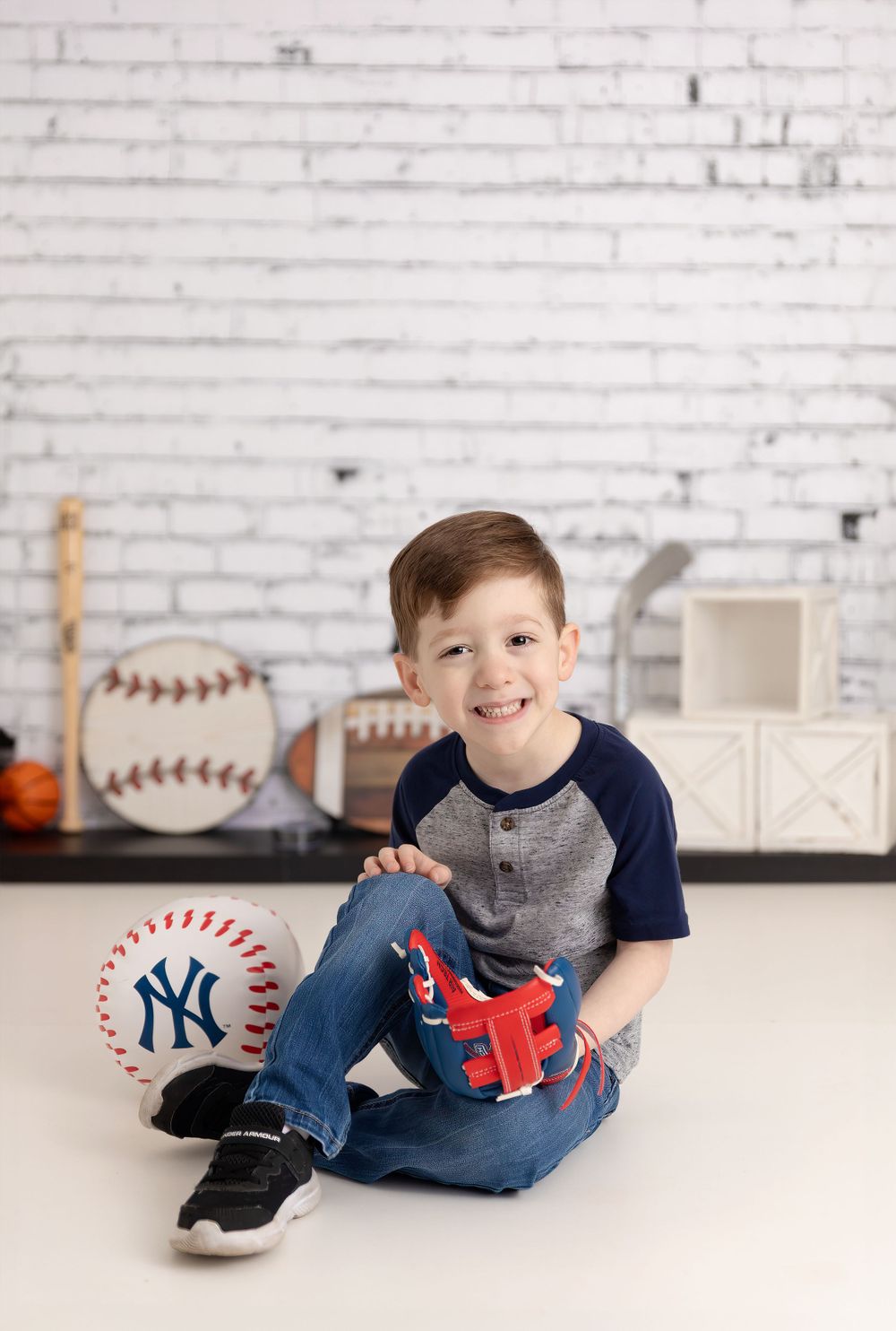 Baseball themed photo shoot with decorative sports props and white brick wall backdrop.