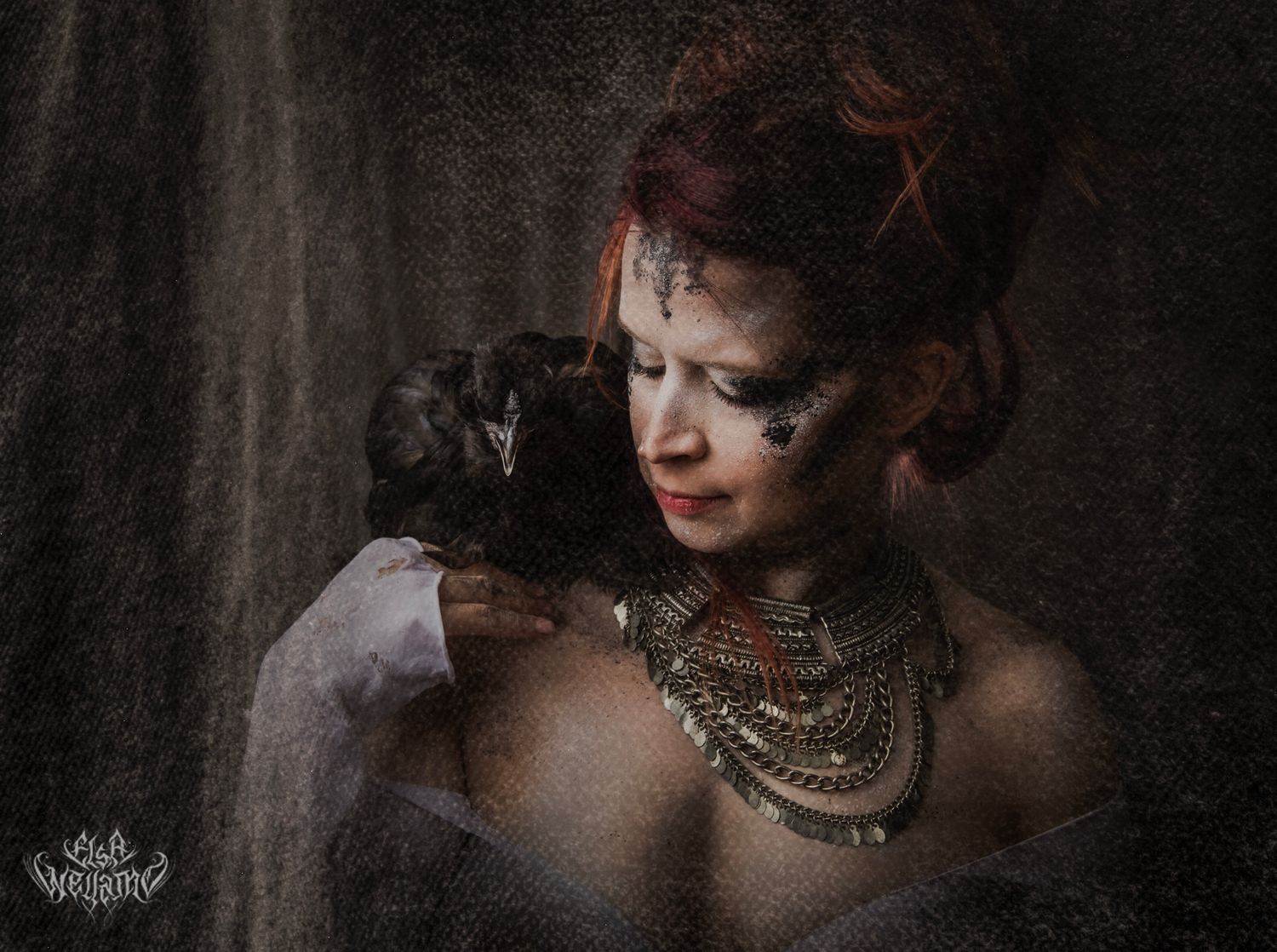 A dramatic vintage-style portrait in dark moody lighting features ornate gold necklaces and elegant styling.