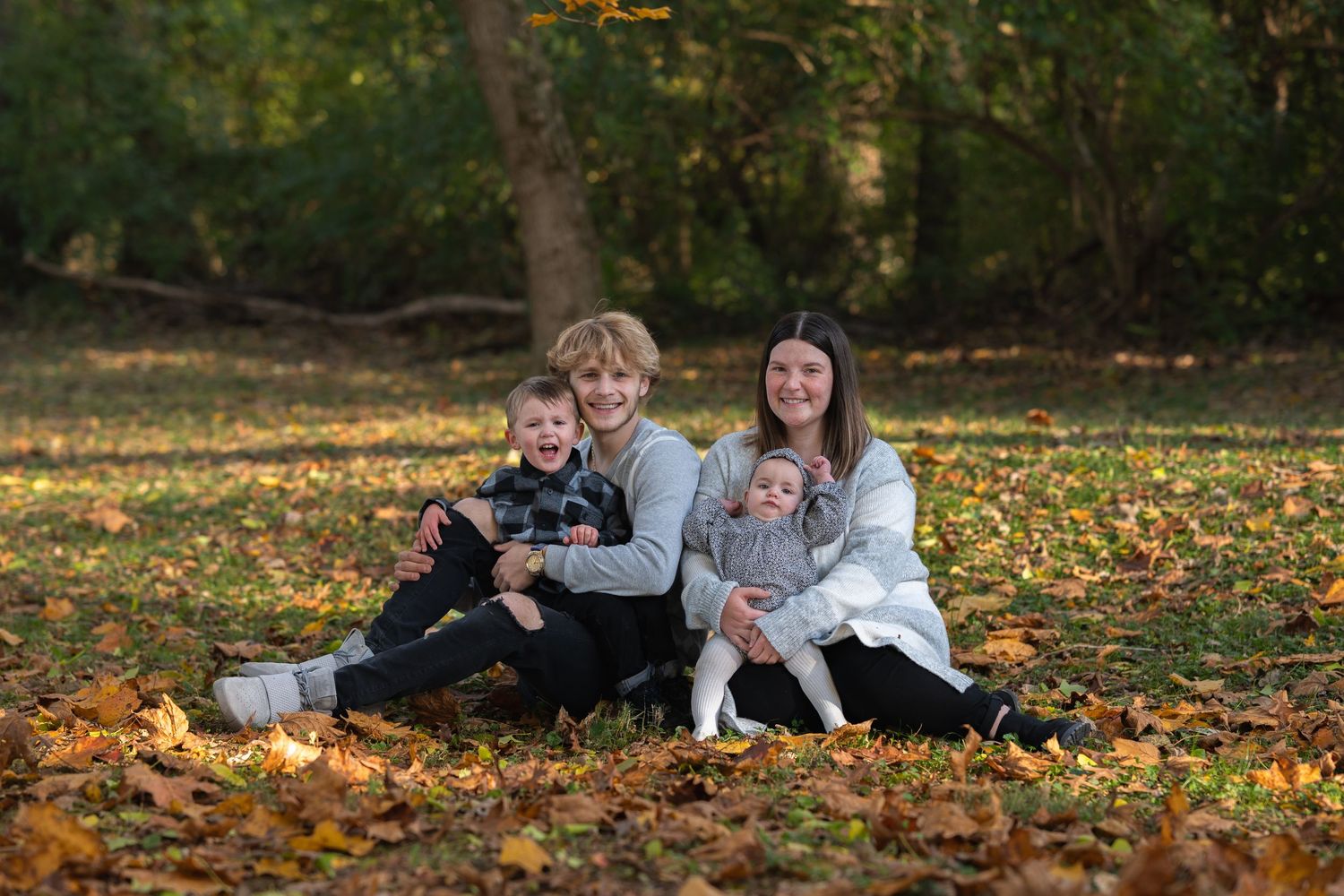 Group relaxing together on autumn ground covered in fallen yellow leaves during outdoor photo session.