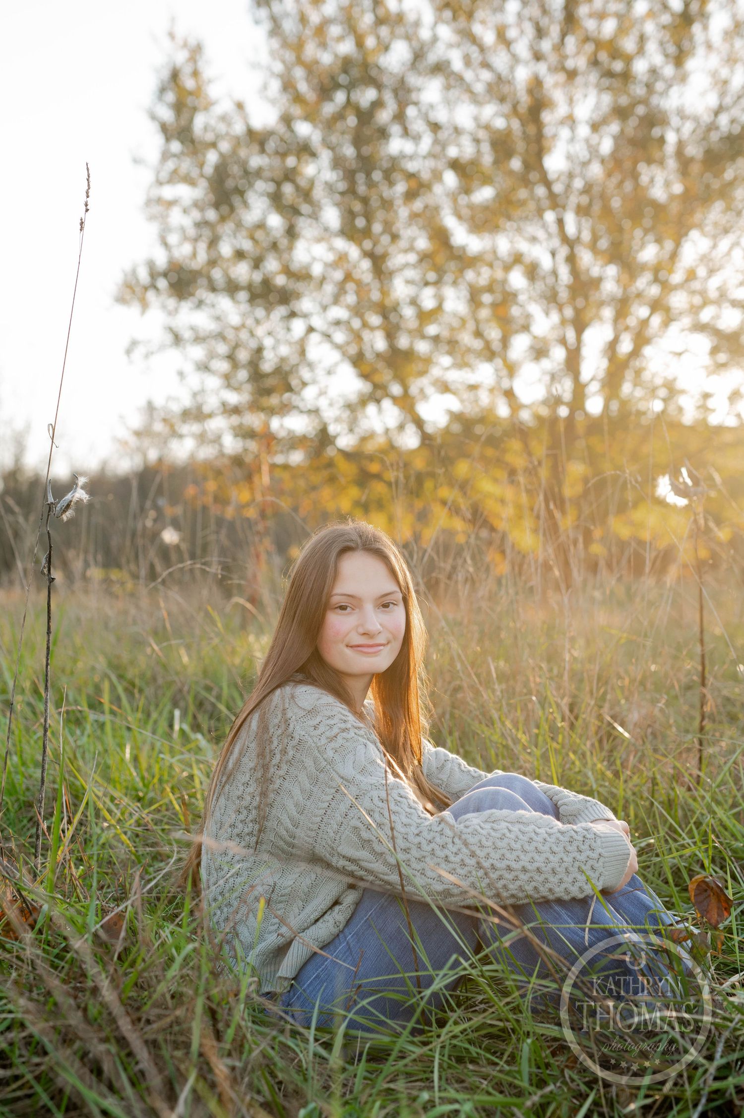 A person in a cozy sweater sits in tall grass during golden hour.