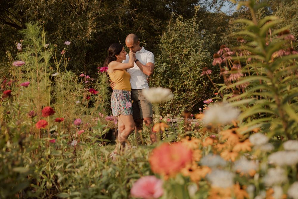 Couple standing among community garden flowers at Lake Ontario, Kingston, ON, Ca. He kisses her hand.