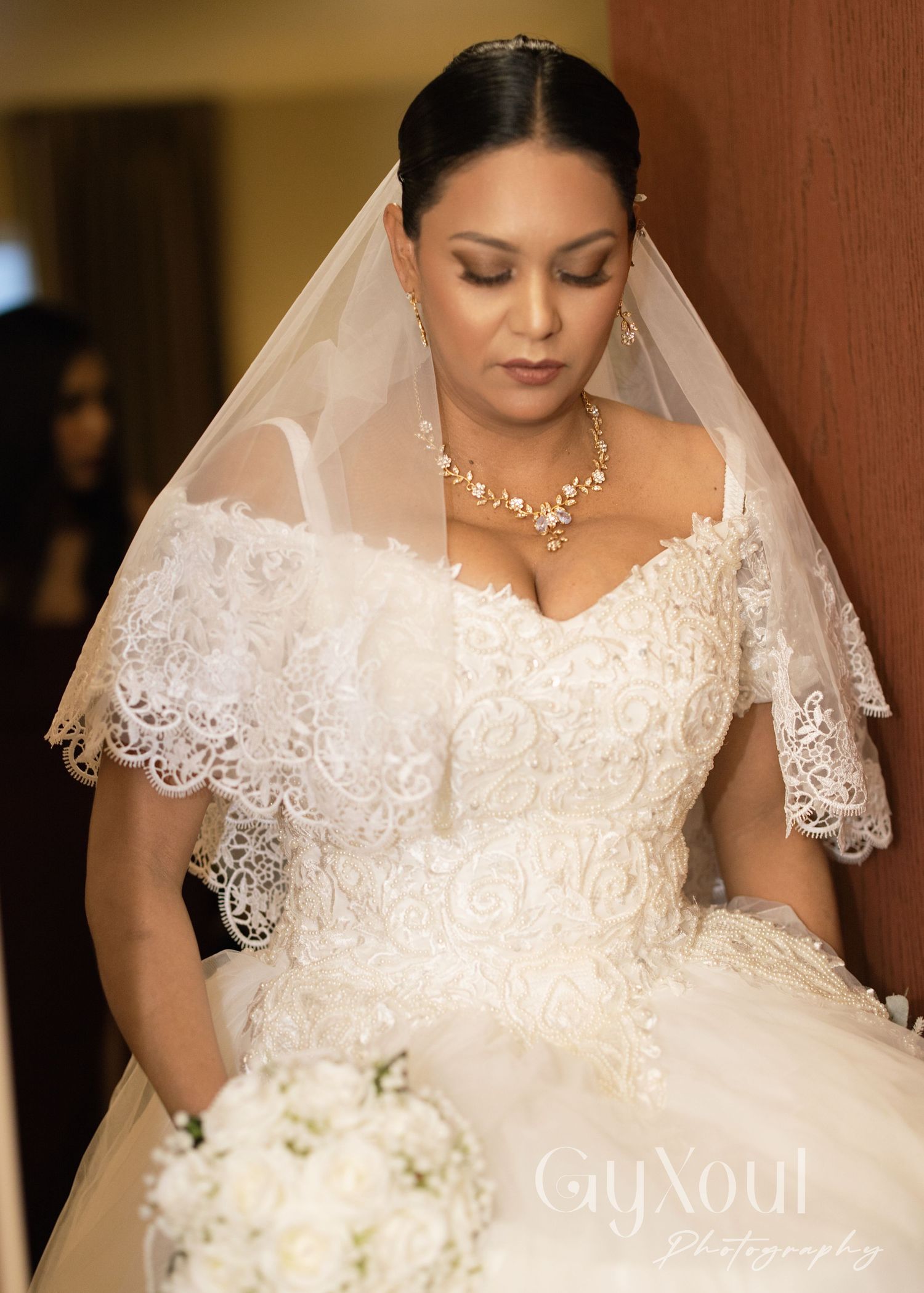 Elegant bride in lace wedding gown with delicate veil and crystal necklace.