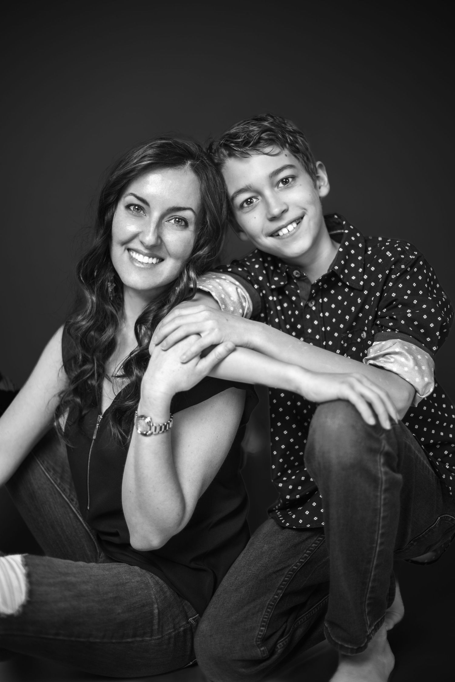 Black and white portrait of two people smiling and posing casually together against a dark background.
