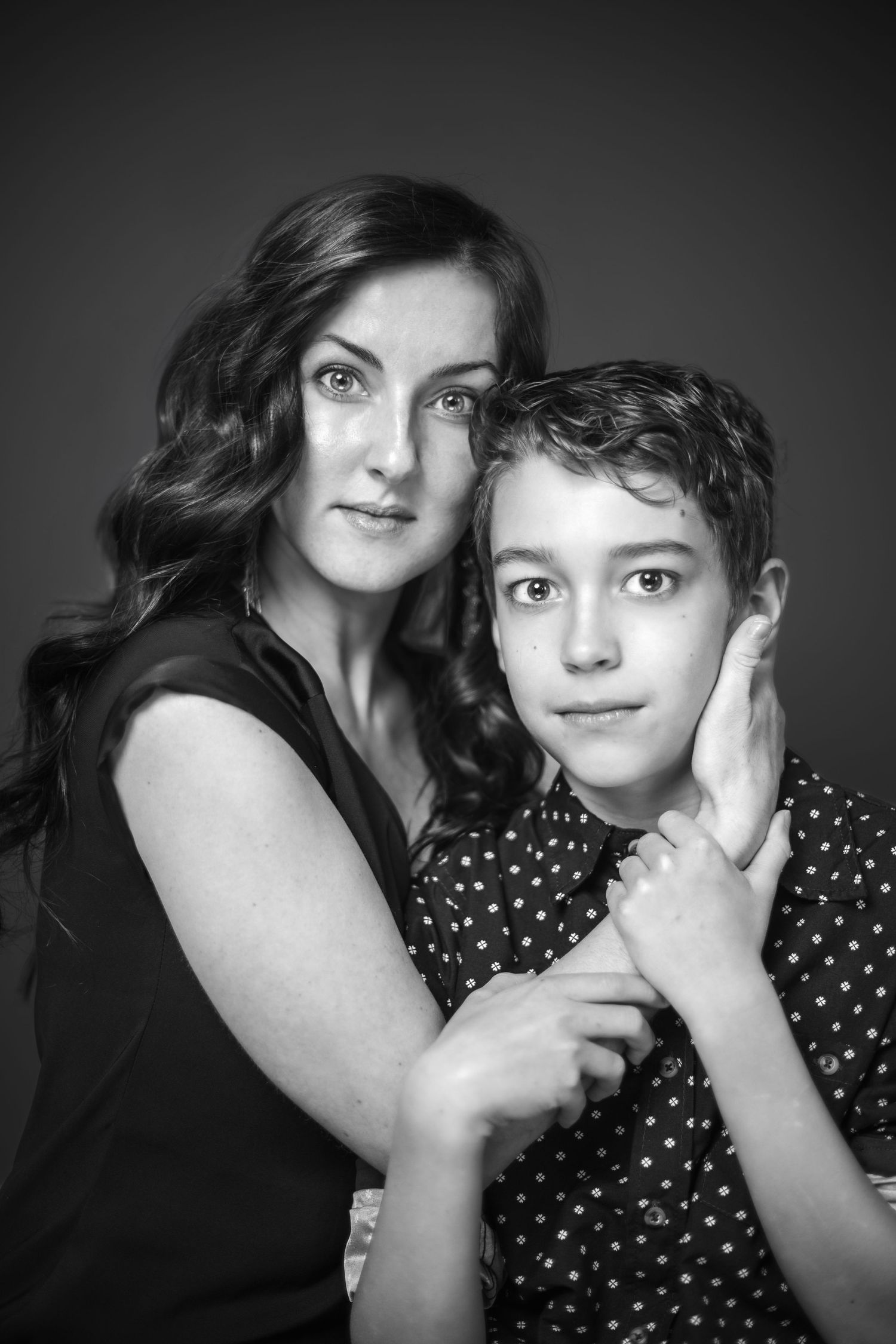 A tender black and white portrait of a parent and child embracing against a dark background.
