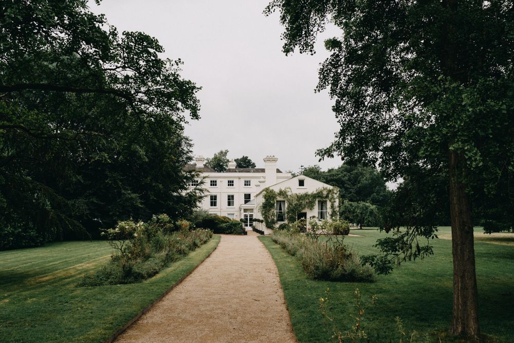 Morden Hall London, a grand white mansion with manicured gardens and a winding gravel path leading through lush green grounds.