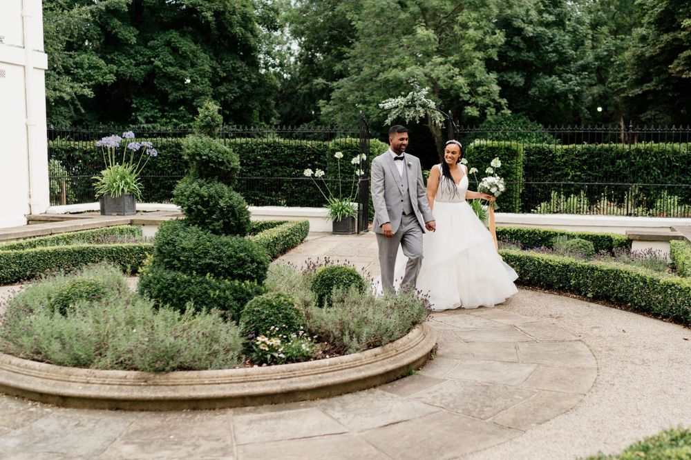 Wedding couple standing together in an elegant formal garden of London Morden Hall with manicured shrubs and curved stone pathways.