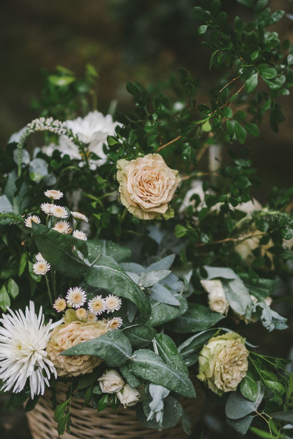 Delicate floral arrangement with peach roses and white flowers among green foliage in muted lighting.