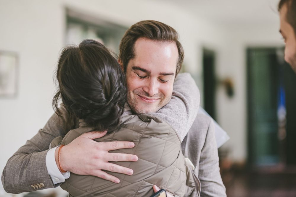 Two people share an emotional embrace, with one person smiling warmly while hugging in a domestic setting.