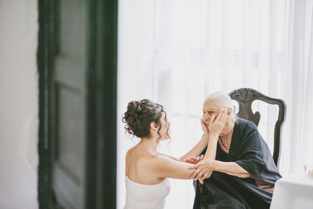 Two people share an emotional moment near a window in an intimate indoor setting during a wedding preparation.