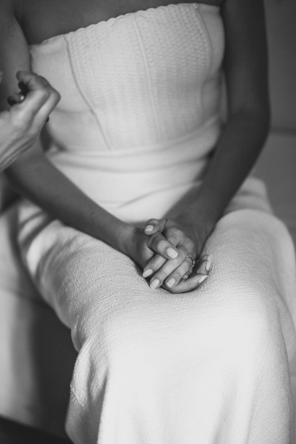 Black and white close-up of hands clasped together while wearing an elegant white dress.